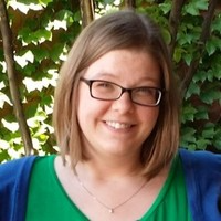 Person with short dark blonde straight hair, glasses, fair skin, and green and blue shirt.